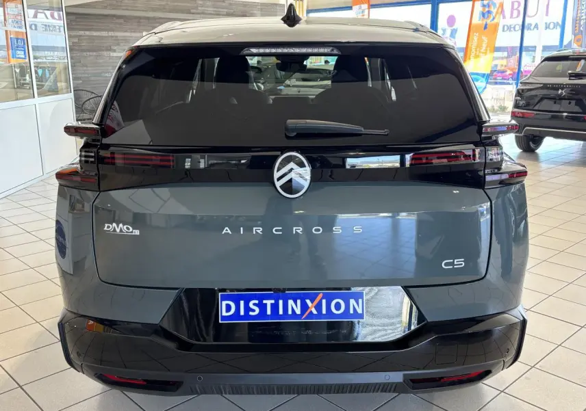 Vue arrière d'un Citroën C5 Aircross vert métallisé avec bandeau noir brillant et feux arrière LED 3D en intérieur showroom.