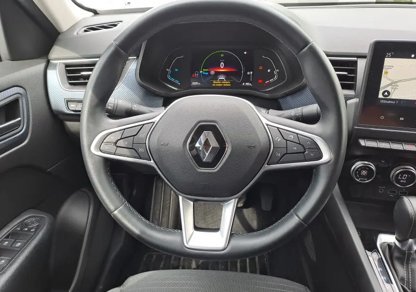 Vue rapprochée du volant noir de la Renault Arkana 2023 avec tableau de bord numérique et écran tactile de navigation.