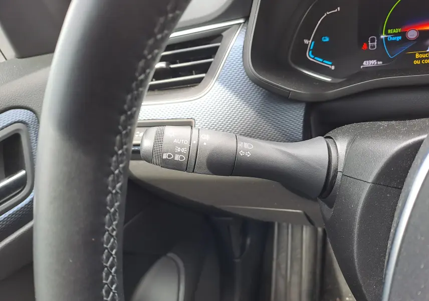 Gros plan sur la commande des phares à gauche du volant dans l'habitacle noir du Renault Arkana hybride 2023.