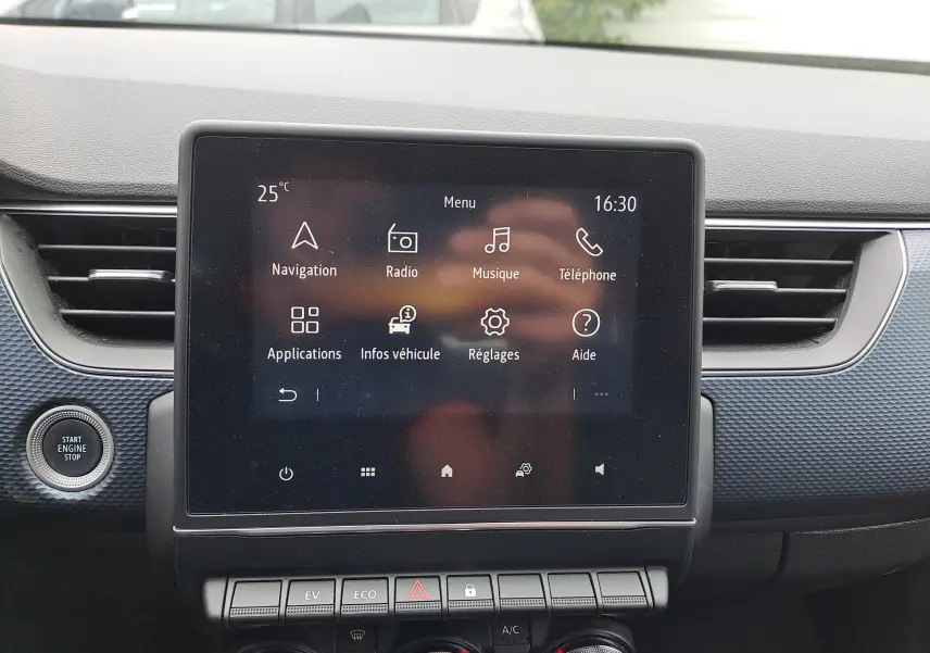 Écran tactile central du tableau de bord du Renault Arkana bleu Zanzibar, avec commandes climatisation et démarrage moteur visible.