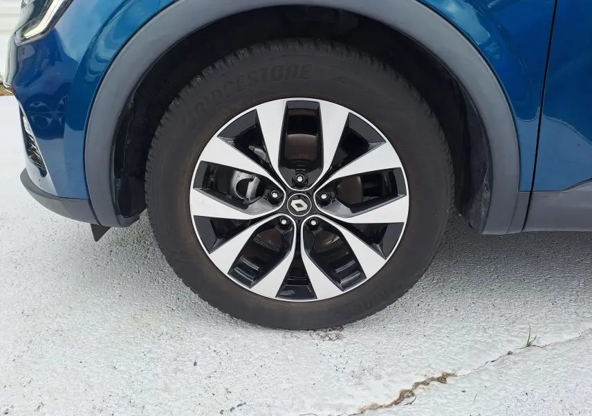 Gros plan sur la roue avant gauche du Renault Arkana bleu Zanzibar métal avec jante alliage bicolore et logo central Renault.