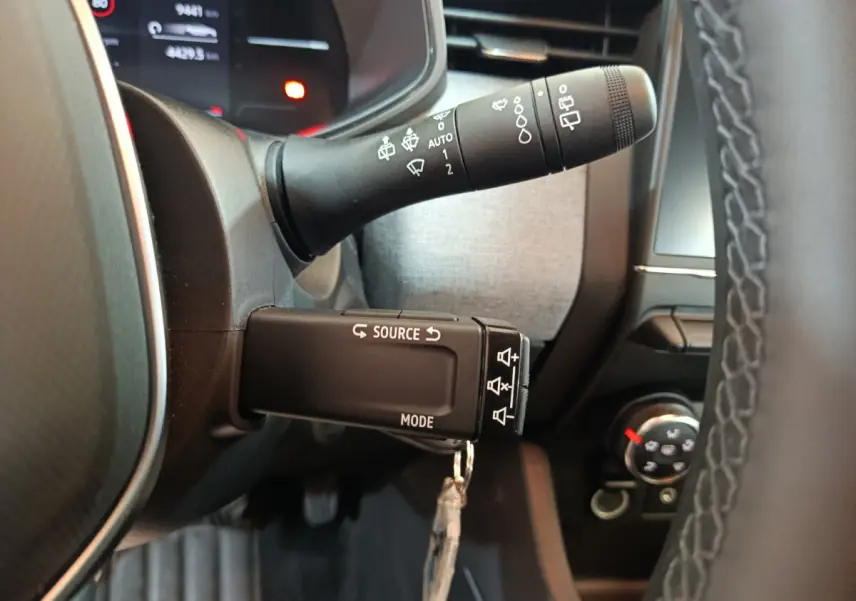 Gros plan sur les commandes au volant noir de la Renault Clio Evolution Blue dCi 100 2025, avec affichage numérique en arrière-plan.