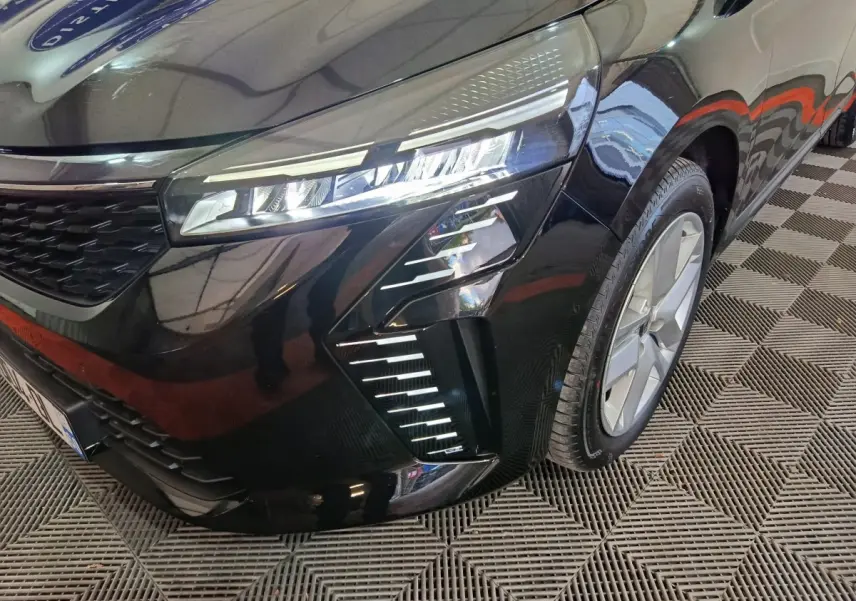 Vue 3/4 avant droit d'une Renault Clio noire 2025 avec phares LED et jantes alliage visibles sur sol damier.