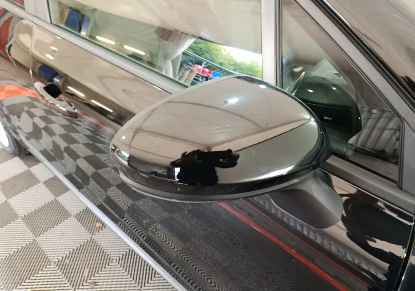 Rétroviseur côté gauche noir brillant de la Renault Clio Evolution Blue dCi 100 vue en gros plan sur fond intérieur.