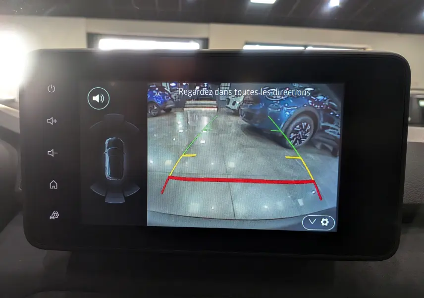 Écran multimédia montrant la caméra de recul du Dacia Sandero Stepway blanc glacier en intérieur, avec lignes de guidage colorées.