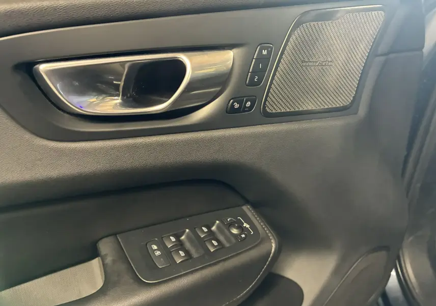 Gros plan sur la porte avant gauche intérieure noire du Volvo XC60 2023 avec commandes et haut-parleur Harman Kardon.