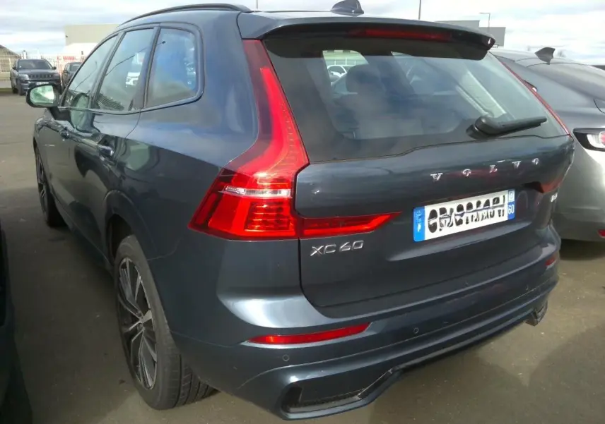 Vue frontale d’un Volvo XC60 bleu avec calandre noire laquée et phares allumés en intérieur showroom.