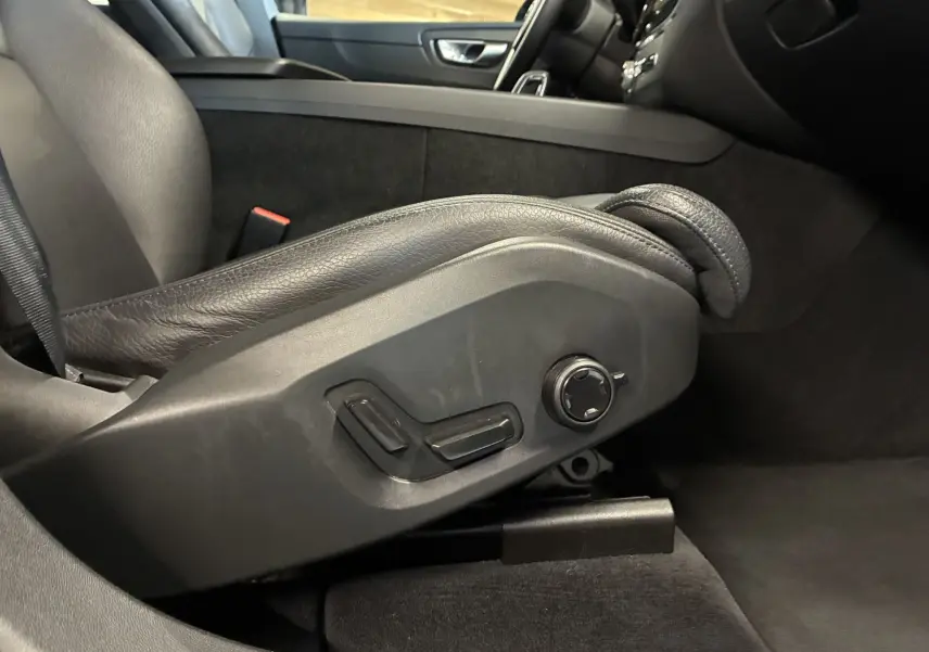 Gros plan sur les commandes électriques du siège avant gauche en cuir noir dans l’habitacle du Volvo XC60 bleu 2023.