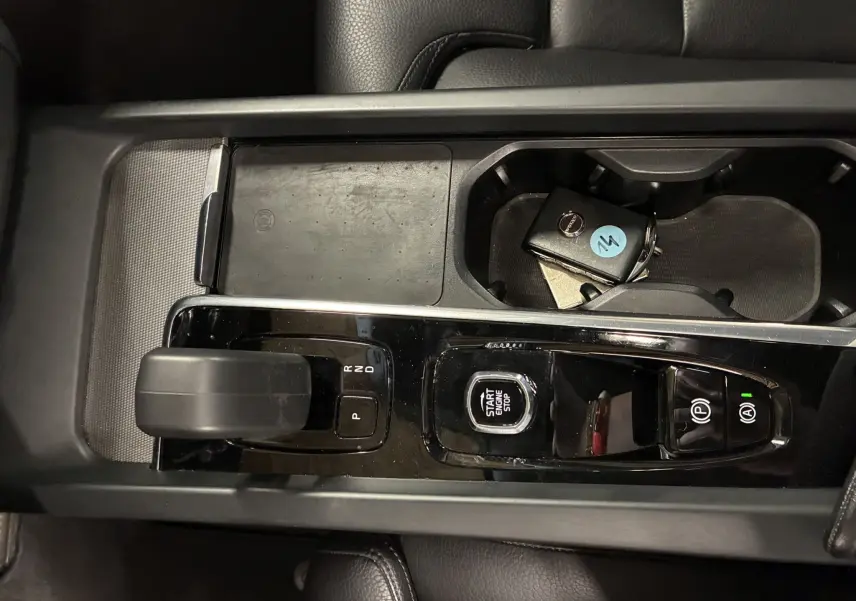 Vue plongeante sur la console centrale noire brillante du Volvo XC60 avec levier de vitesse et clé dans porte-gobelets.