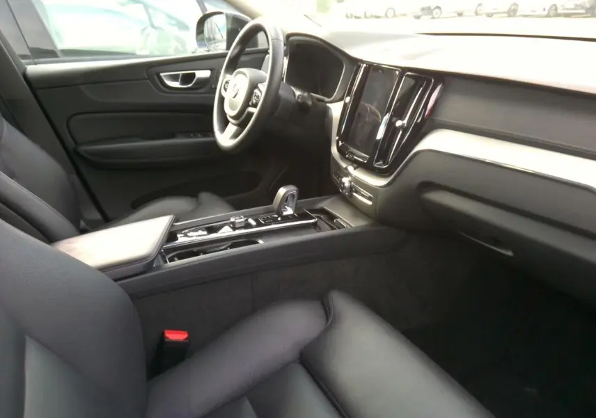 Vue arrière d’un Volvo XC60 bleu foncé 2023 avec feux LED allumés et logo distinctif sur un mur bois.