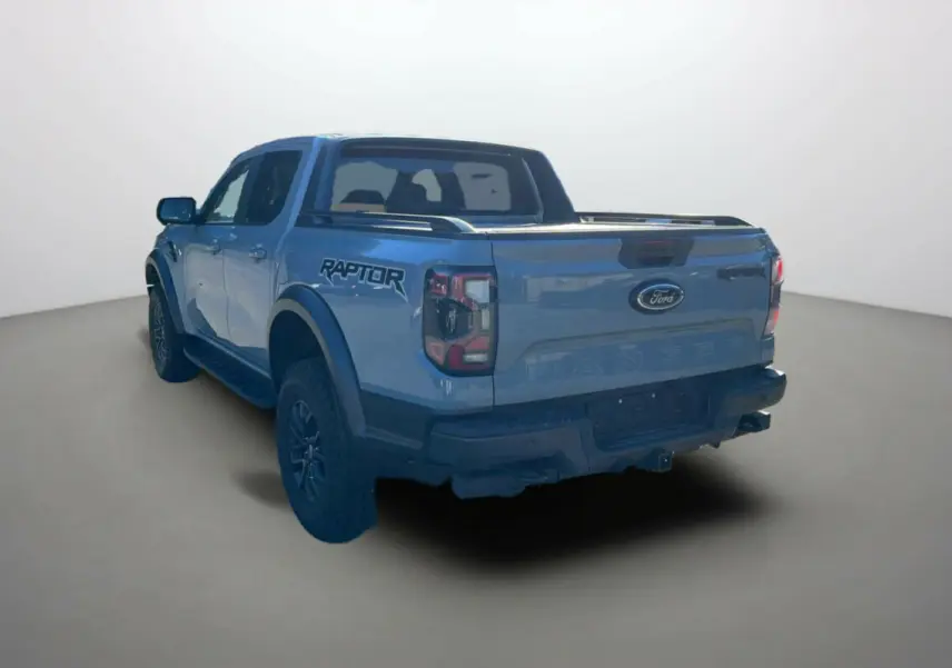 Vue 3/4 arrière du Ford Ranger Raptor gris commandeur avec logo Raptor sur la benne et jantes alu noires.