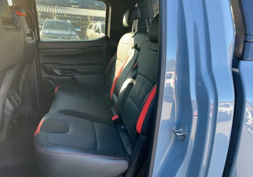Vue intérieure arrière côté droit du Ford Ranger Raptor 2026 gris commandeur, sièges cuir noirs avec surpiqûres rouges.