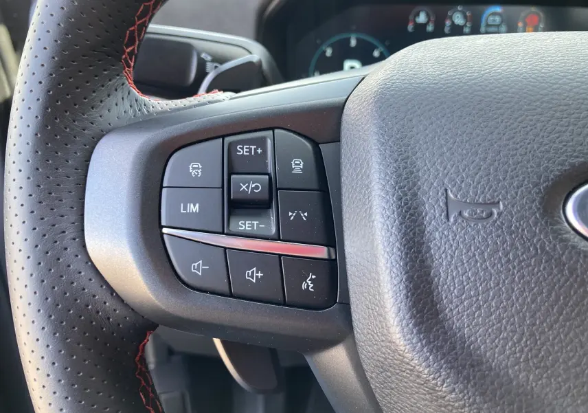 Gros plan sur le volant cuir perforé gris du Ford Ranger Raptor 2026, avec commandes multifonctions et surpiqûres rouges.