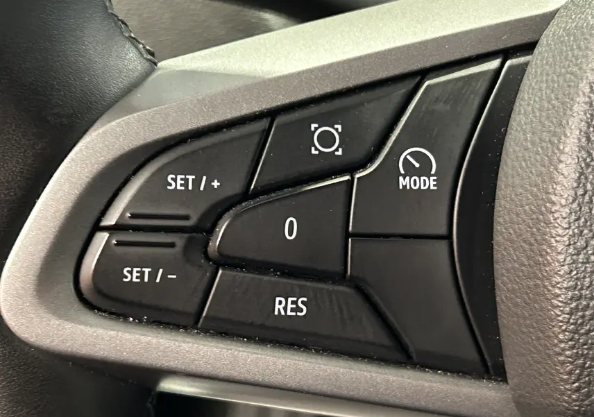 Gros plan sur les commandes noires du volant du Dacia Duster 2024, boutons de réglage et mode visibles.