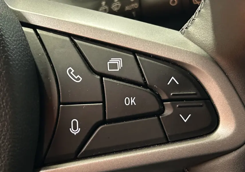 Gros plan sur les commandes multifonctions noires du volant du Dacia Duster 2024, finition Sandstone.