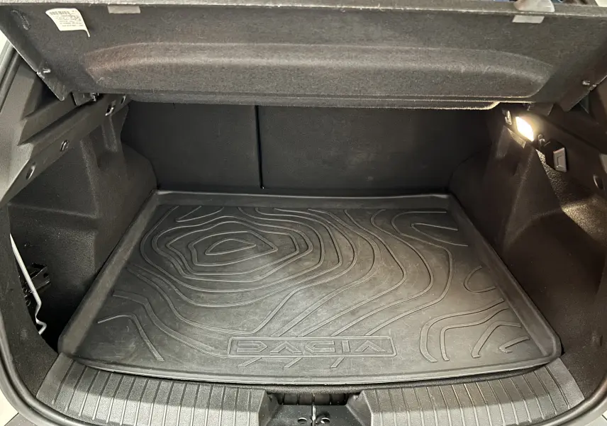 Coffre ouvert du Dacia Duster 2024 avec tapis de sol noir texturé et éclairage intérieur à droite.