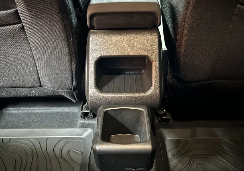 Vue rapprochée du rangement central arrière noir entre les sièges arrière du Dacia Duster 2024, intérieur sombre.