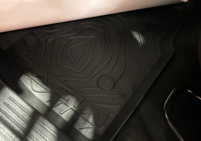 Tapis de sol noir avec logo Dacia en gros plan, côté passager avant du Dacia Duster 2024 couleur Sandstone.