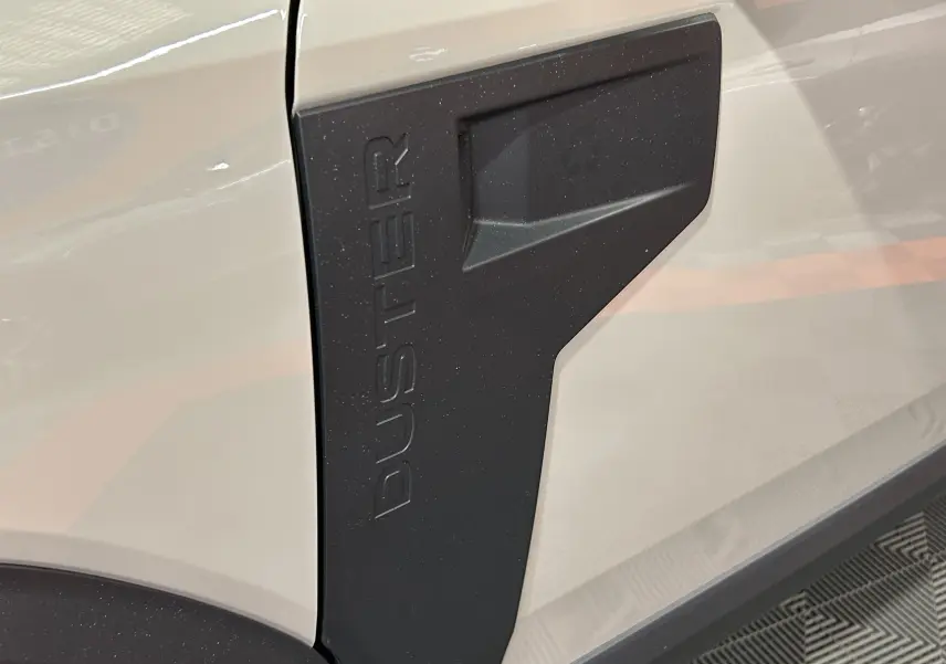 Gros plan sur l’écusson noir « DUSTER » sur la carrosserie beige sandstone du SUV Dacia Duster 2024.