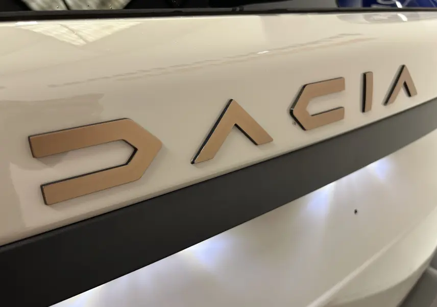 Gros plan sur le logo DACIA en relief couleur sable sur la porte arrière blanche du Duster 2024.