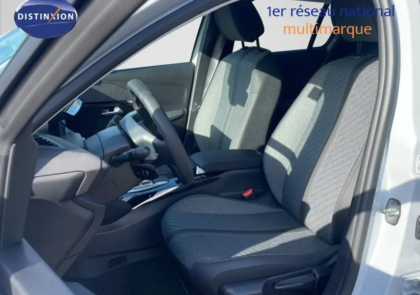 Vue intérieure côté conducteur de la Peugeot 208 Hybrid blanche, montrant les sièges en tissu gris et le volant multifonction.