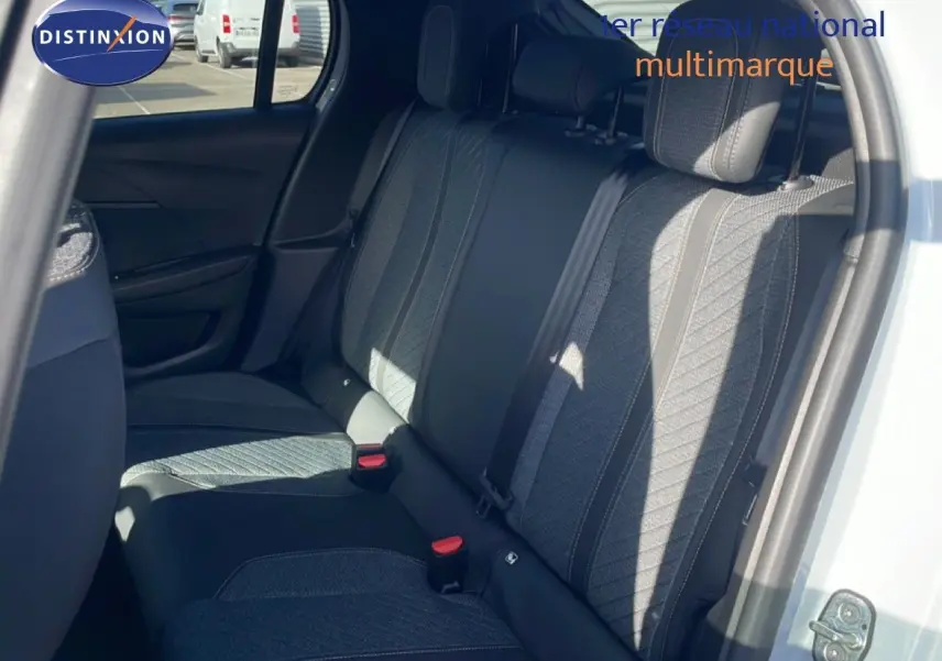 Vue intérieure côté droit montrant la banquette arrière en tissu gris avec surpiqûres, porte ouverte d'une Peugeot 208 blanche.