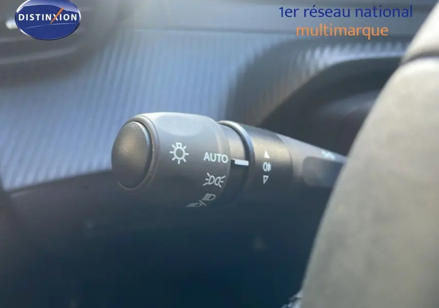 Gros plan sur la commande des phares automatique à gauche du volant dans une Peugeot 208 blanche hybride 2026.