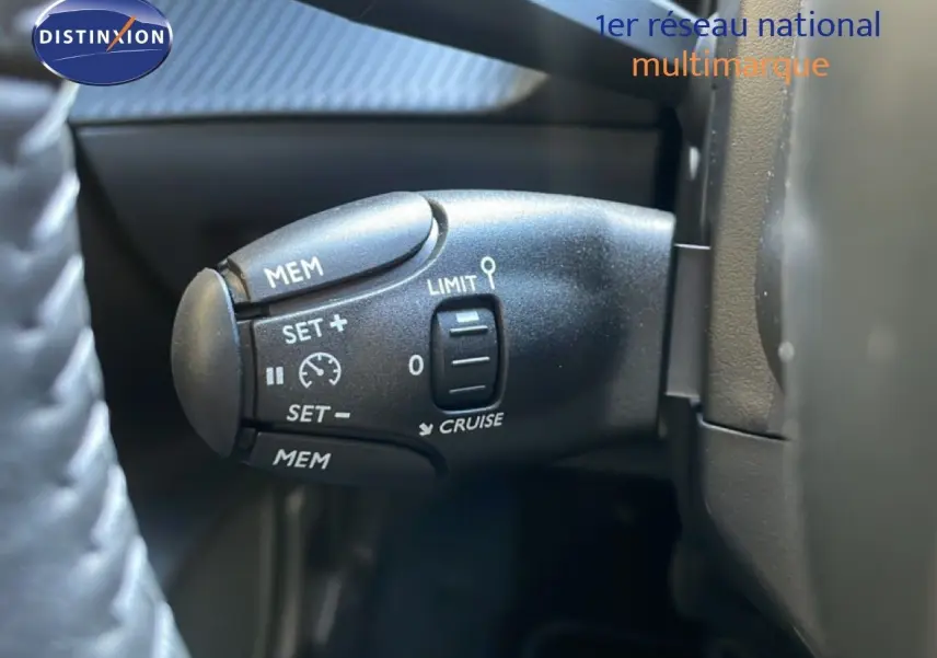 Gros plan sur la commande de régulateur de vitesse à gauche du volant dans une Peugeot 208 blanche hybride 2026.