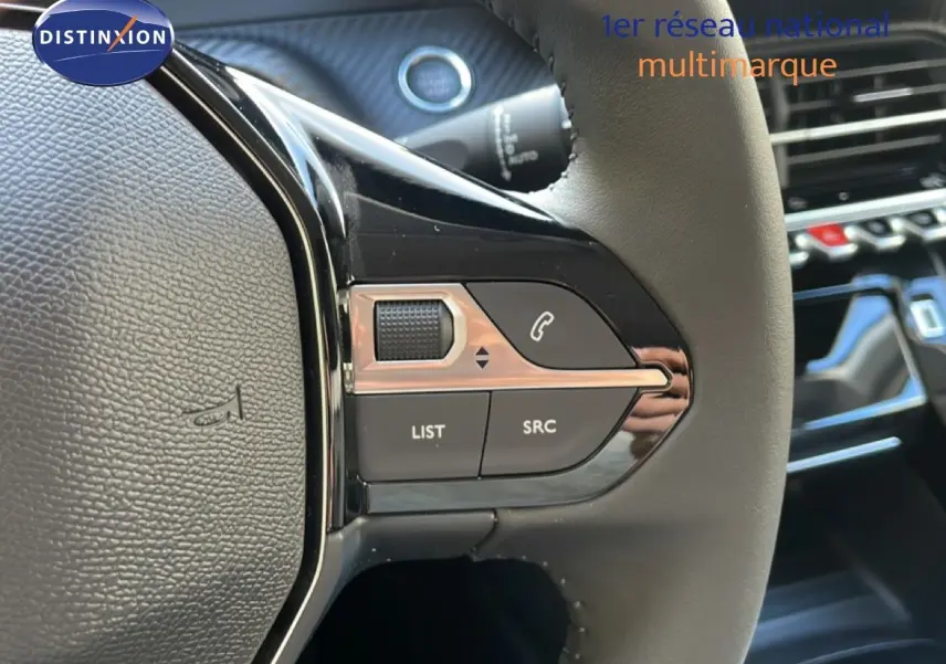 Gros plan sur les commandes gauche du volant cuir noir d’une Peugeot 208 Hybrid blanche, avec tableau de bord en arrière-plan.