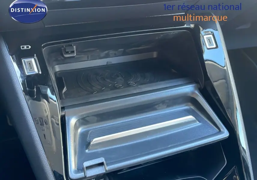 Gros plan sur la console centrale noire brillante de la Peugeot 208 Hybrid 110ch avec compartiment ouvert et prises USB visibles.