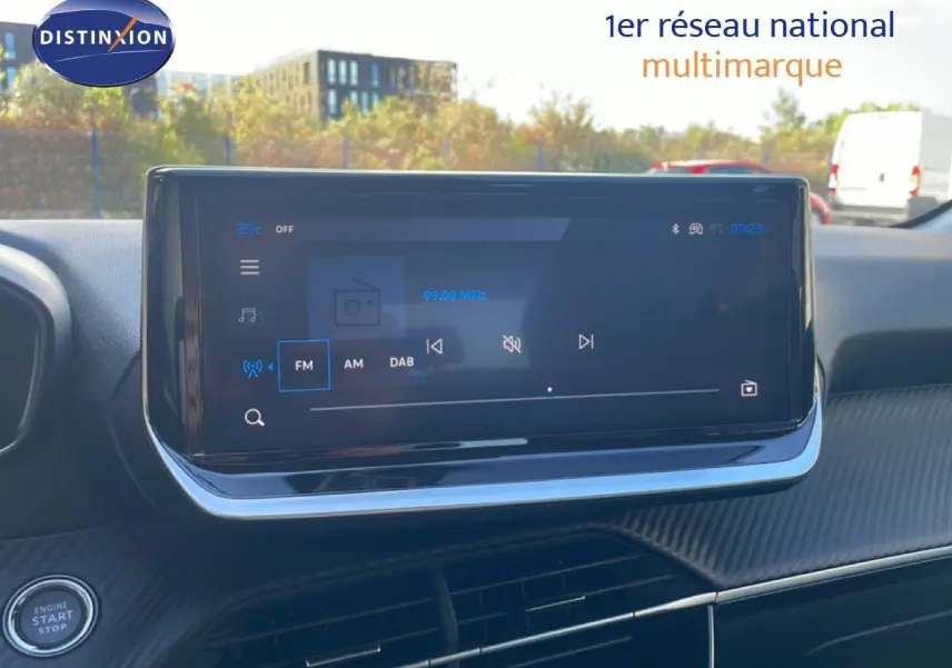 Écran tactile central du tableau de bord d’une Peugeot 208 hybride blanche, affichant la radio FM à 99 MHz.