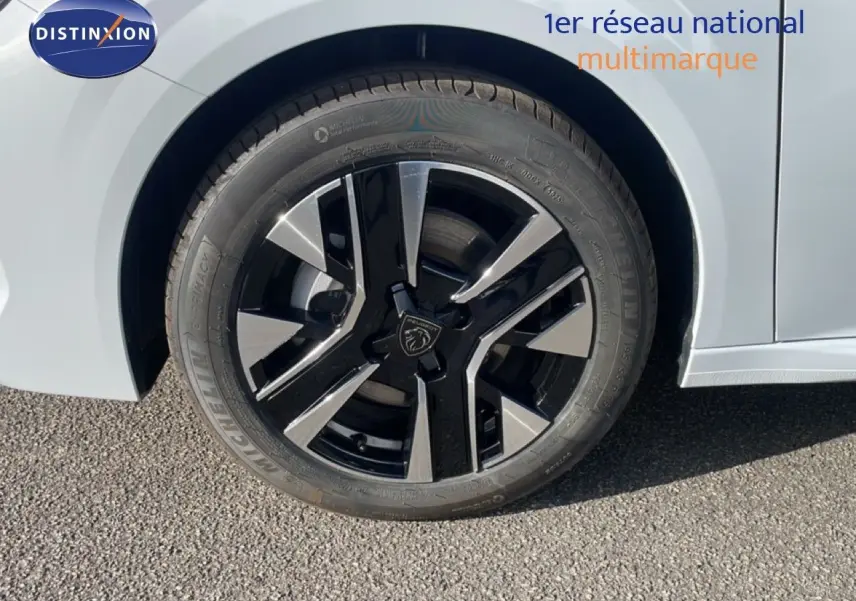 Gros plan sur la roue avant gauche d’une Peugeot 208 blanche, jante alliage noire et argentée au design moderne.