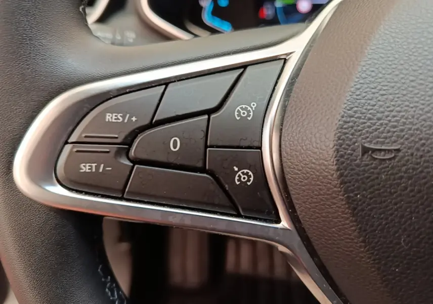 Gros plan sur les commandes du régulateur de vitesse du volant en cuir synthétique d'une Renault Clio Business E-TECH 140 blanche.