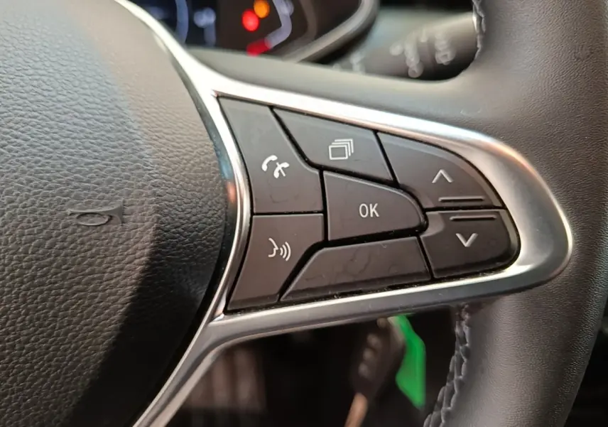 Gros plan sur les commandes multifonctions à droite du volant cuir synthétique de la Renault Clio Business E-TECH 140 blanche.