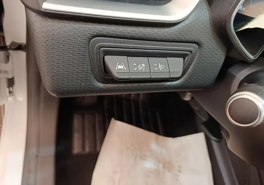 Gros plan sur les commandes d’aide à la conduite sous le tableau de bord d’une Renault Clio blanche, côté conducteur.