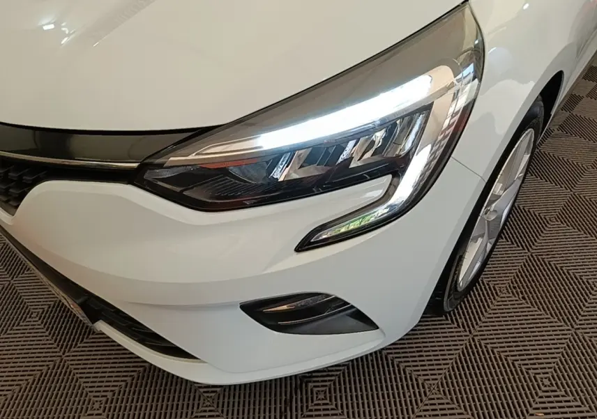 Gros plan sur l'avant droit de la Renault Clio Business E-TECH blanche, mettant en valeur son phare LED allumé et la calandre.