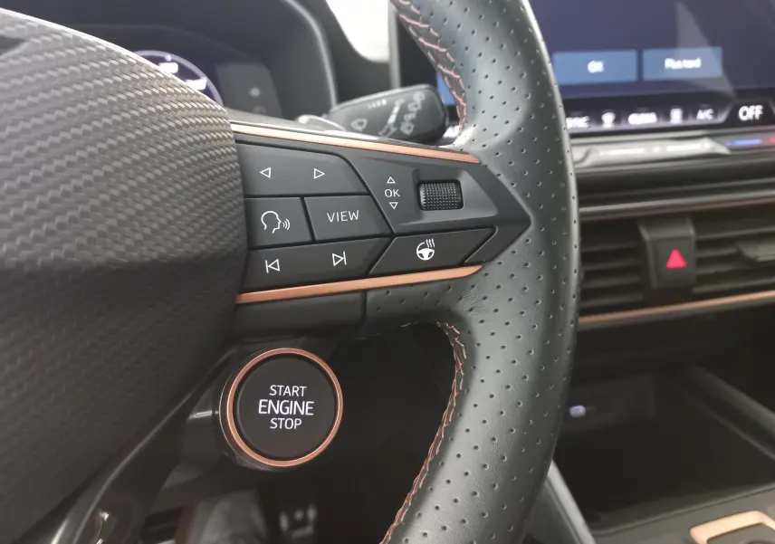 Gros plan sur le volant perforé noir avec surpiqûres cuivrées et bouton Start Engine Stop d'une CUPRA Leon Blanc Nevada 2025.
