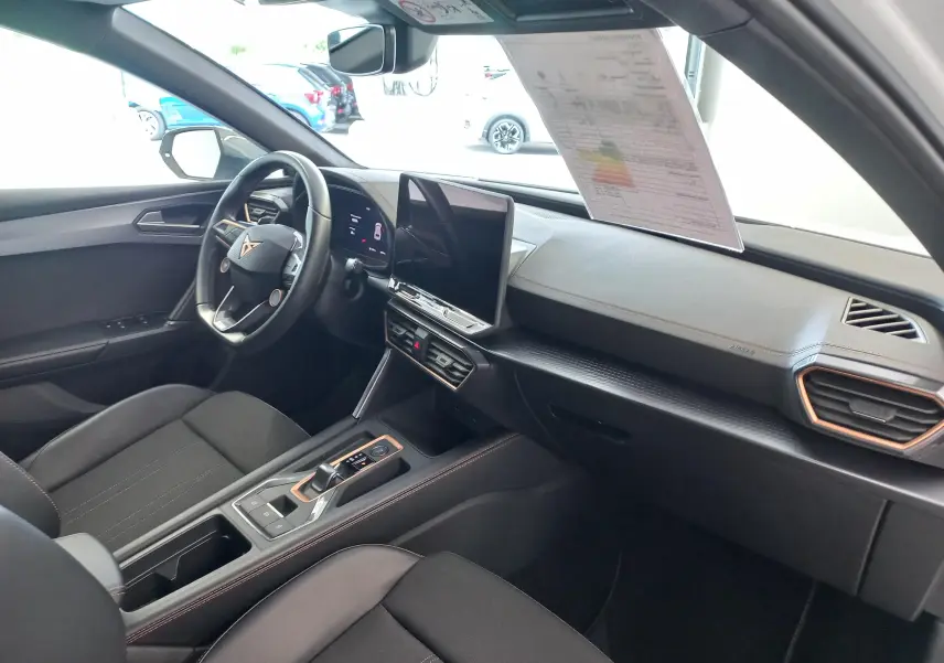 Vue intérieure côté conducteur de la CUPRA Leon 2025, tableau de bord noir avec écran tactile central et volant multifonction.