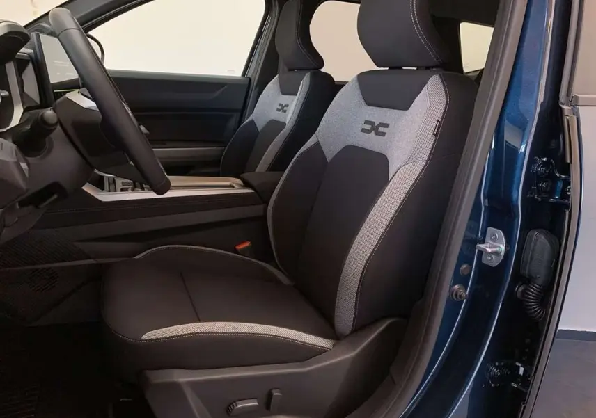 Vue intérieure côté conducteur du Dacia Bigster Hybrid 155 Journey Plus 2026, sièges tissu noir et gris avec logo X brodé.