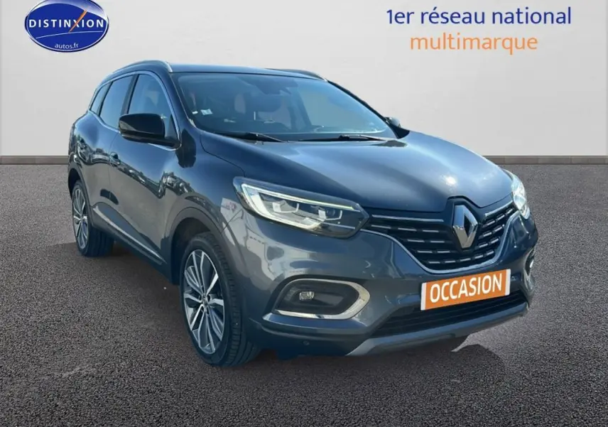 Renault Kadjar gris foncé en 3/4 avant droit avec jantes alliage 19 pouces et barres de toit visibles.