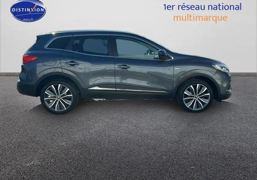 Profil côté droit du Renault Kadjar gris foncé 2019 avec jantes alliage 19 pouces et barres de toit visibles.