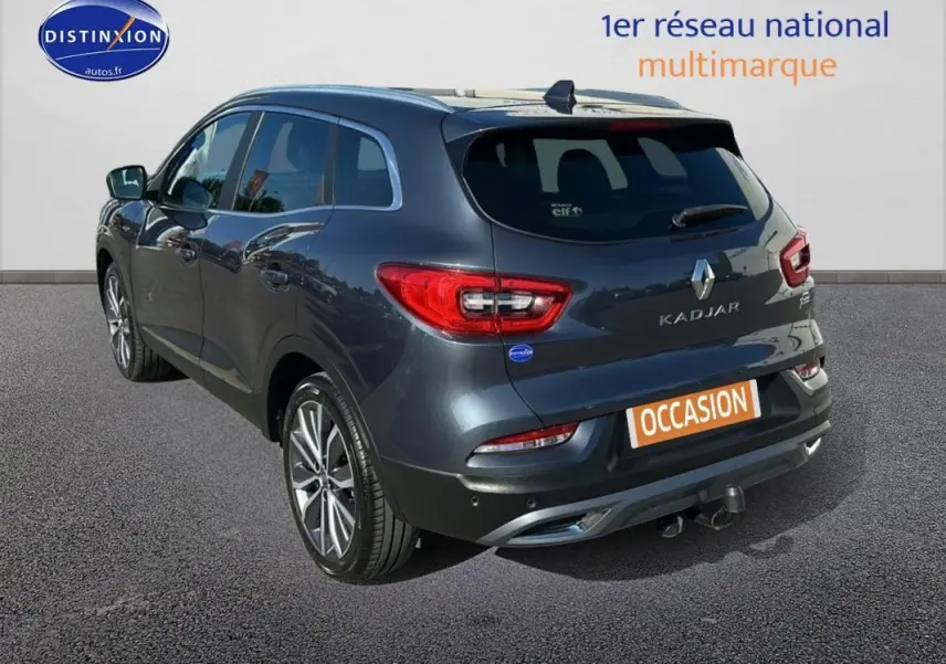 Vue 3/4 arrière gauche d'un Renault Kadjar gris foncé avec jantes alliage 19 pouces et barres de toit visibles.