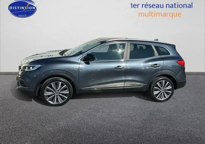 Renault Kadjar gris foncé vu de profil côté gauche avec jantes alliage 19 pouces et barres de toit visibles.