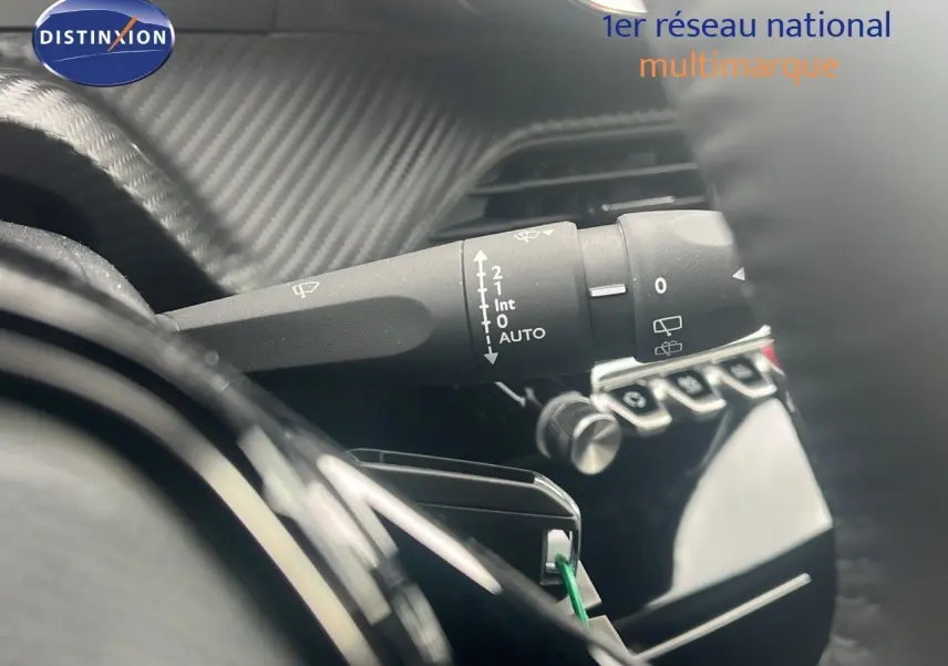 Gros plan sur la commande d'essuie-glace à gauche du volant dans l'habitacle d'un Peugeot 2008 blanc Okenite Metal.