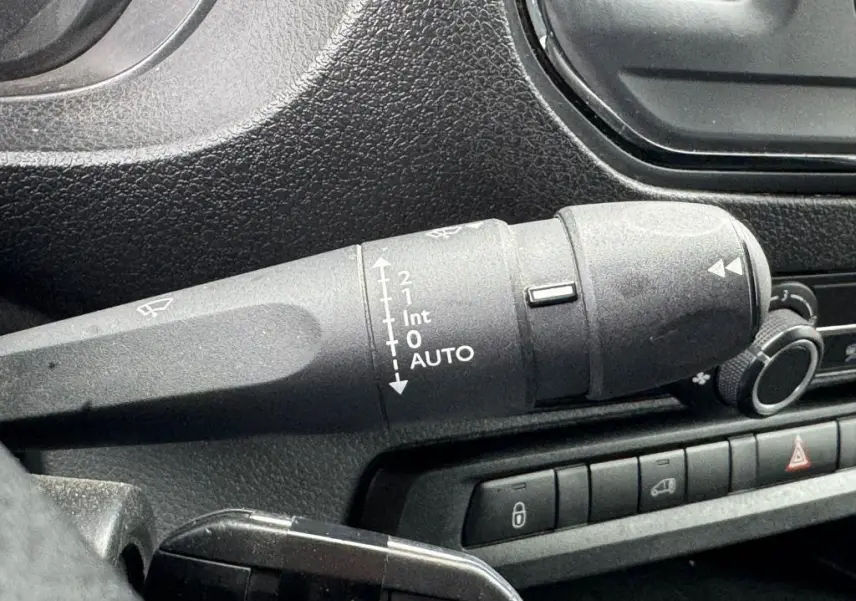 Gros plan sur la commande des essuie-glaces à gauche du volant dans l'habitacle noir du Peugeot Expert Fourgon blanc.