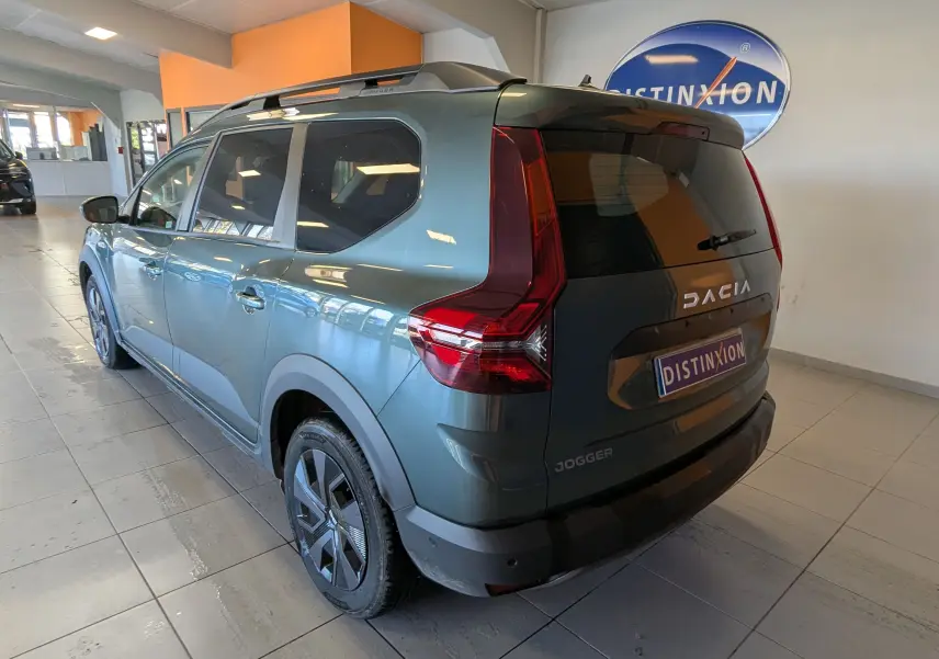 Vue 3/4 arrière droite d'un Dacia Jogger vert cèdre métal 2025 en intérieur, avec feux arrière caractéristiques et jantes noires.