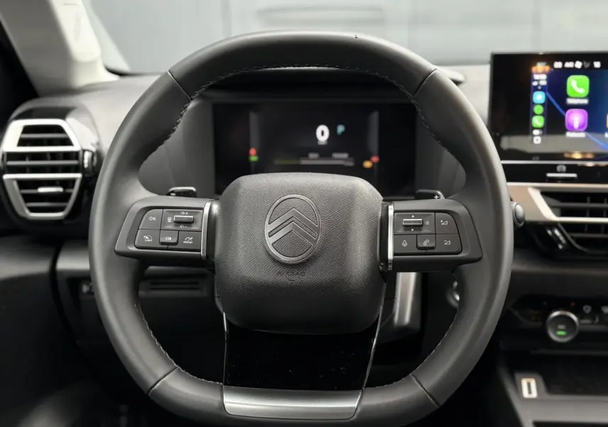Vue rapprochée du volant cuir noir de la Citroën C4 2025 avec commandes intégrées et tableau de bord numérique.