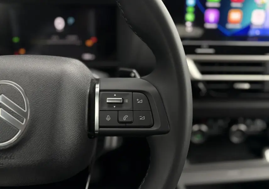 Gros plan sur les commandes au volant cuir noir de la Citroën C4 Hybrid 2025 avec écran tactile en arrière-plan flou.