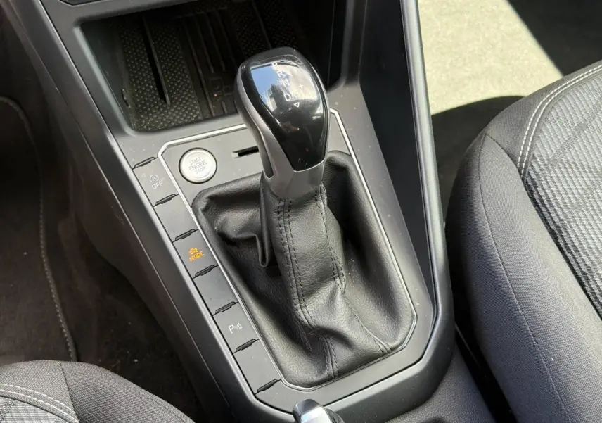 Gros plan sur le levier de vitesses automatique noir et gris du Volkswagen Taigo 1.0 TSI R-Line, avec siège tissu gris visible.