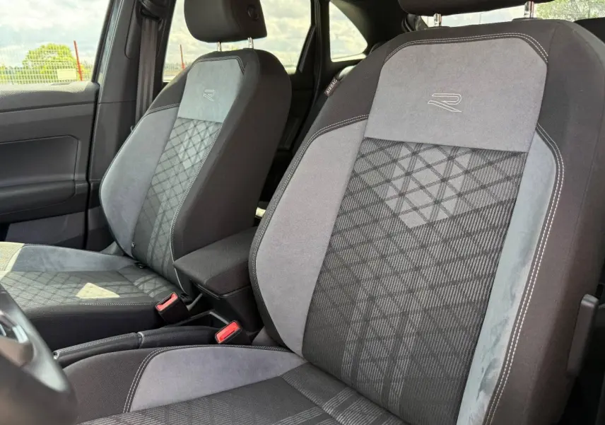 Vue intérieure rapprochée des sièges avant gris et noirs en tissu R-Line avec logo brodé sur Volkswagen Taigo 2025.